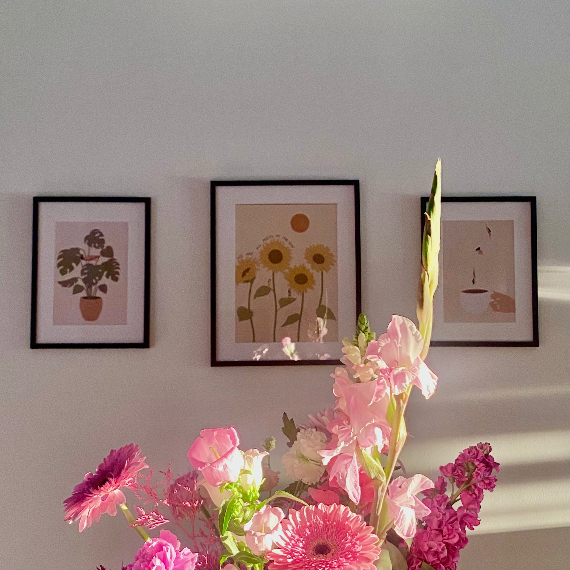 Framed artwork on a wall with a bouquet of pink flowers in the foreground.